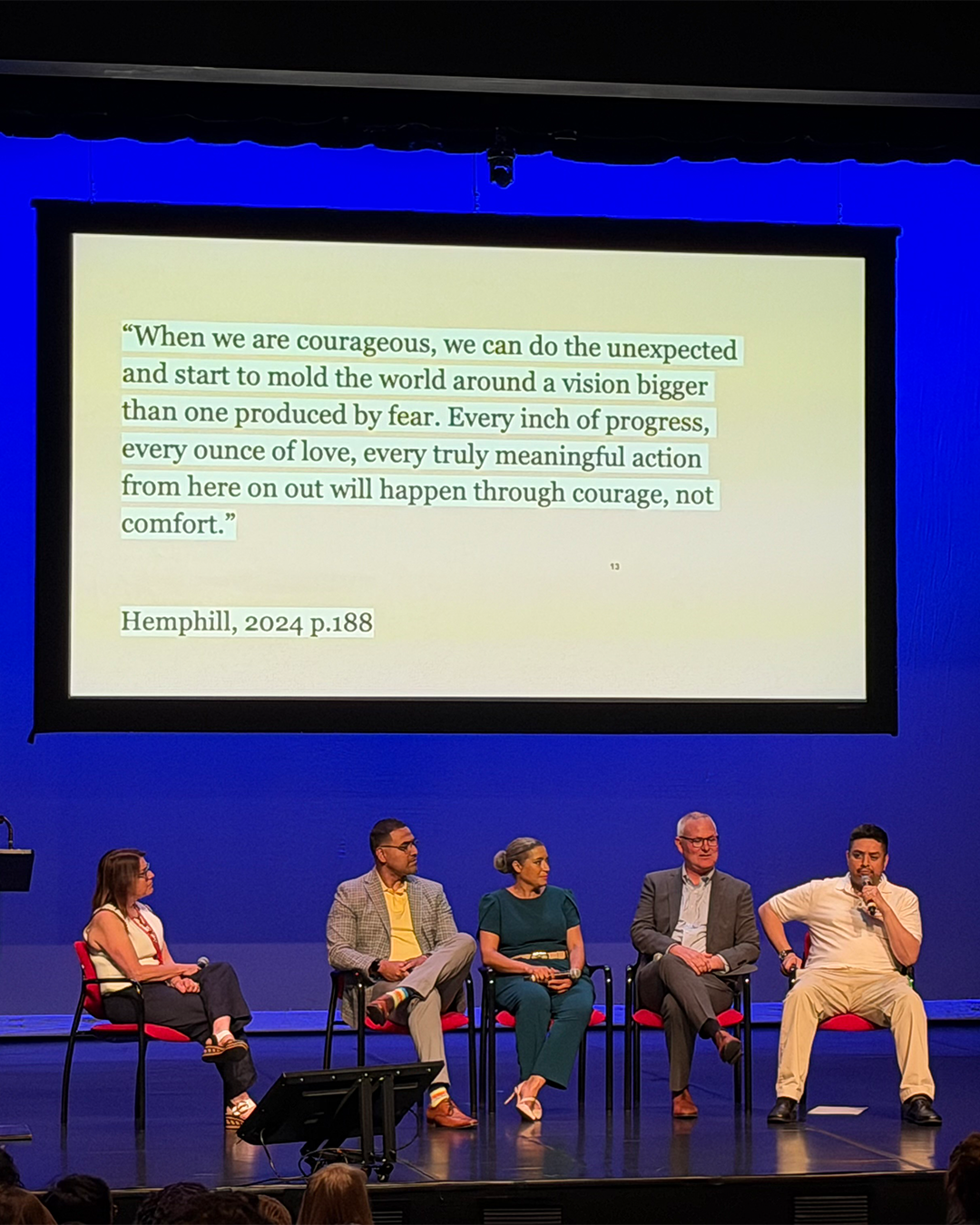 A panel speaking on stage in front of a projected screen